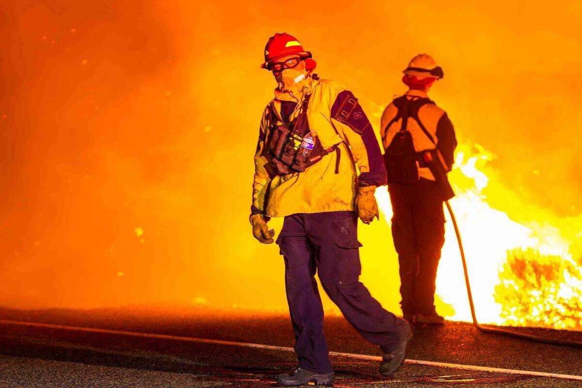 A firefighter walks along the fireline while another crew member monitors advancing flames during the Nine Canyon Fire on Saturday morning near Kennewick. Crews worked through the night as strong winds drove the wildfire toward Finley.