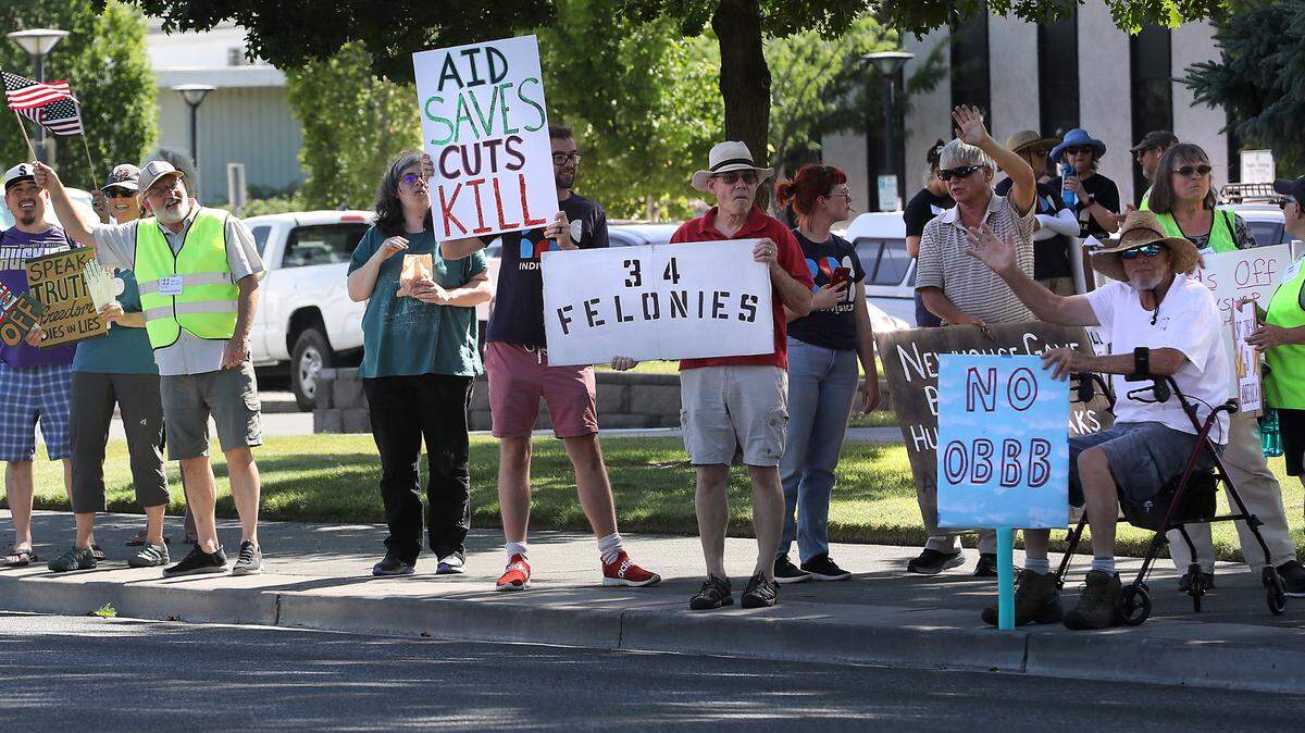 Protesters with Indivisible Tri-Cities stand on the sidewalk along George Washington Way near Richland’s John Dam Plaza to oppose the “One Big Beautiful Bill.”
