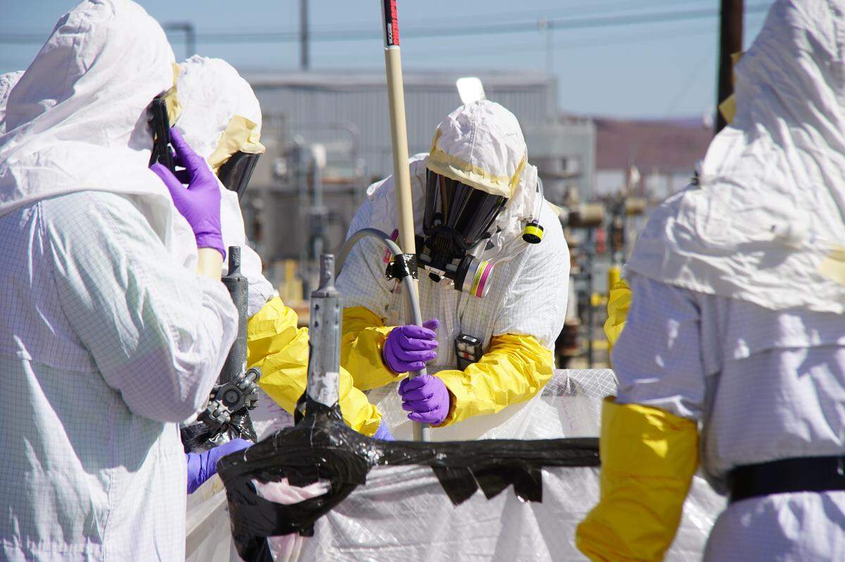 Workers with Hanford Tank Waste Operations & Closure (H2C) use long reach tools to tighten nozzle connectors while installing the final piece of piping needed to connect the tank farms to the vitrification plant.