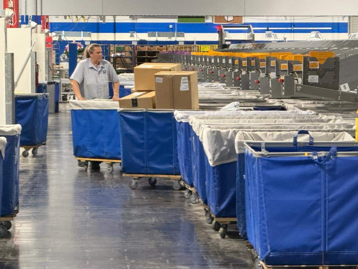 A U.S. Post Office worker pushes a cart full of boxes ready for delivery to Tri-Cities residents at the Pasco Sorting and Delivery Center.