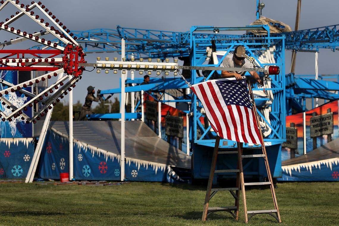 Anthony Ferdick, a Davis Shows Northwest carnival worker, attaches the U.S. Flag to the mast of the Extreme Scream before the drop tower ride is raised into its vertical position. 