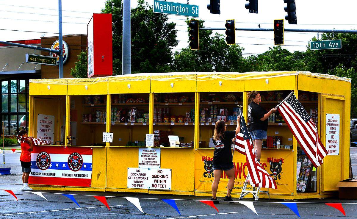 Kaleb Little helps Amanda Youngs and JoLayne Thompson, from left, place U.S. Flags on the family run Young's Fireworks stand at the intersection of South Washington Street and 10th Ave. in Kennewick.