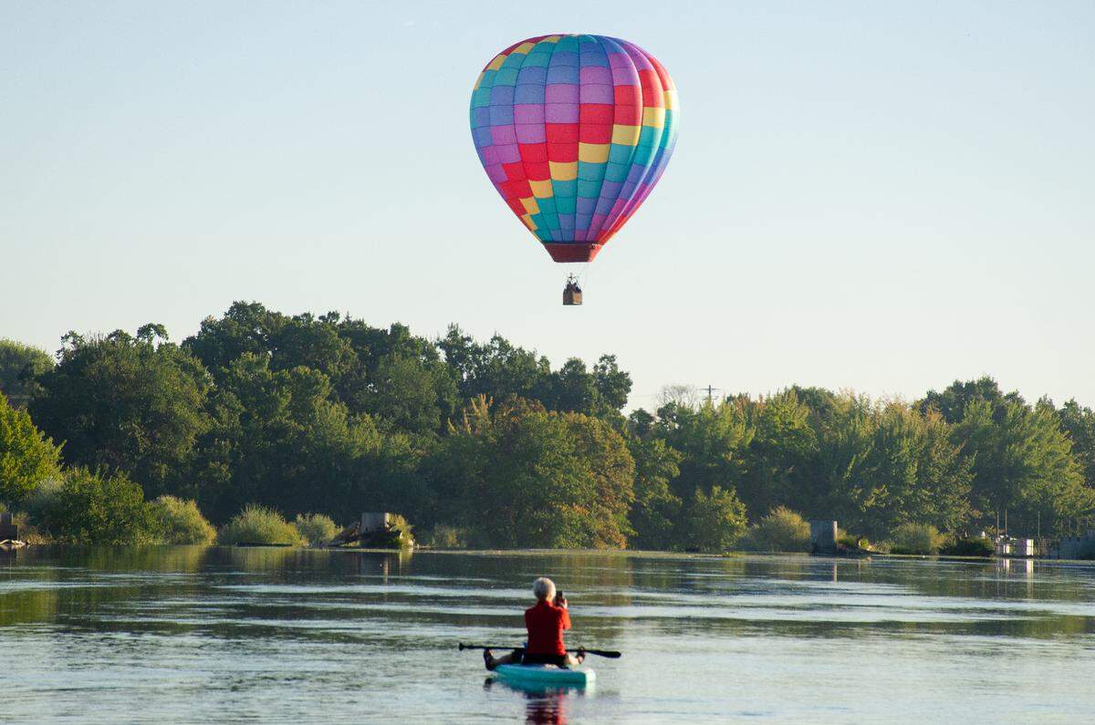 A recreationalist kayaking the lower Yakima River on Friday morning in Prosser stops to take a photo of the Knight-N-Gale hot air balloon during the kickoff of the 33rd annual Great Prosser Balloon Rally.