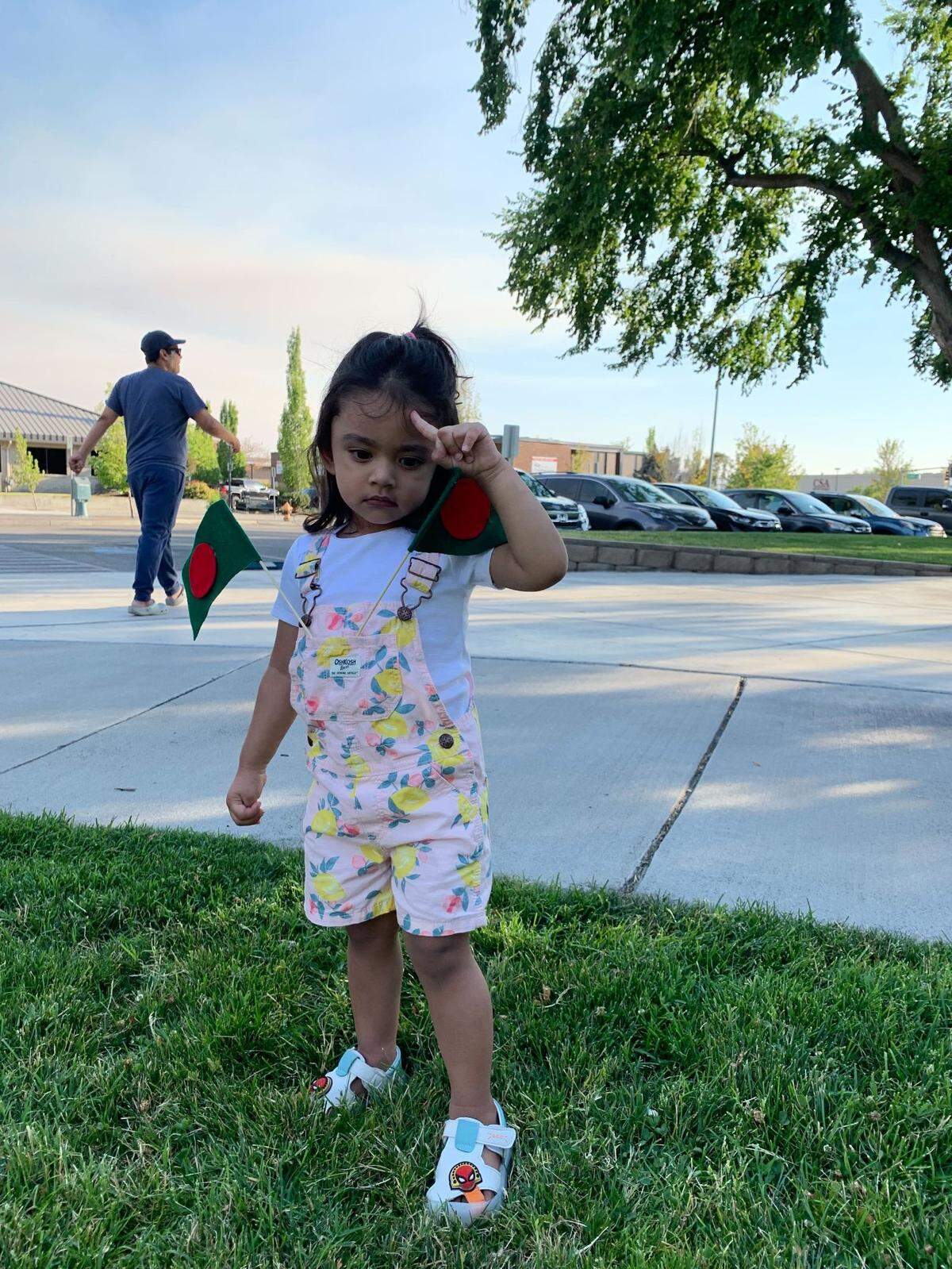 A young member of the local Bangladeshi community, Ezlian, stands near protesters alongside George Washington Way with two small versions of the flag of Bangladesh to spread awareness of the unrest and student killings in Bangladesh.