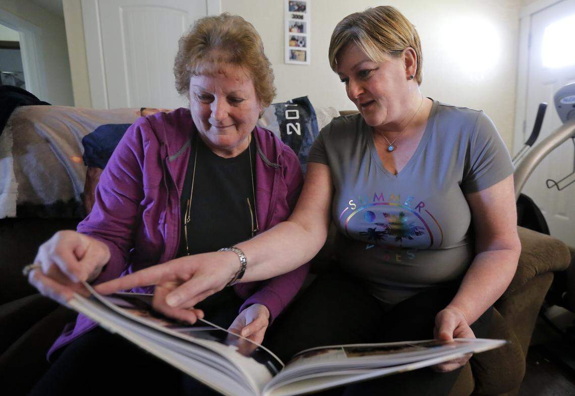 Wanda McCollom, left, and her daughter Heather Escobar, sit inside of their home looking at photos of two of their family members that they lost to suicide. Wanda McCollom lost her son, John McCollom and daughter, Amy McCollom, to suicide.