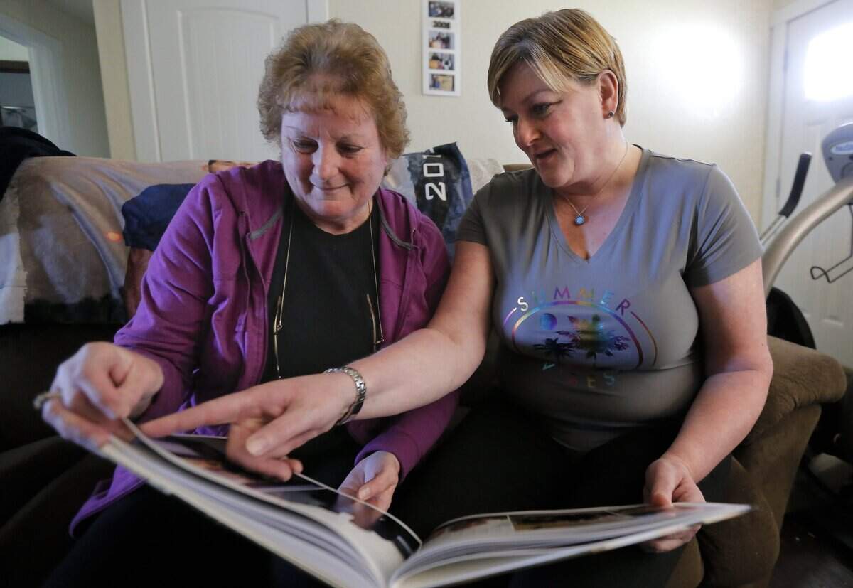 Wanda McCollom, left, and her daughter Heather Escobar, sit inside of their home looking at photos of two of their family members that they lost to suicide. Wanda McCollom lost her son, John McCollom and daughter, Amy McCollom, to suicide.