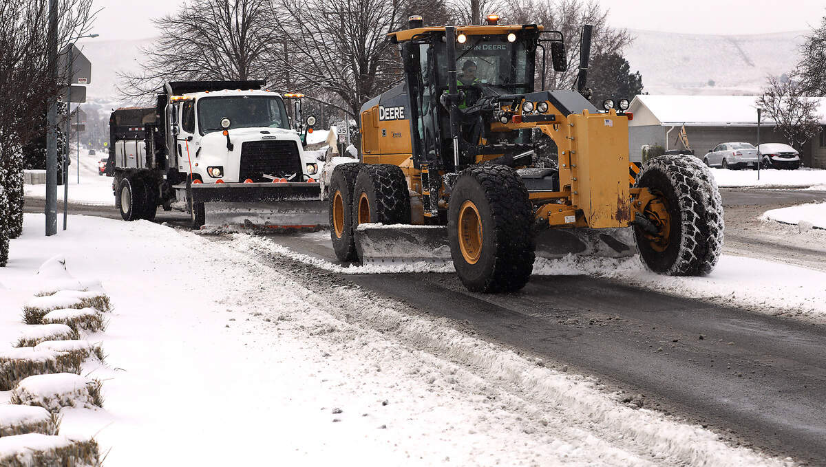 A Kennewick city road grader and snow plow work in tandem clearing snow from the roadway at the roundabout on West 27th Avenue at South Vancouver Street Friday morning following a fresh layer of overnight snowfall that coated the Mid-Columbia region.