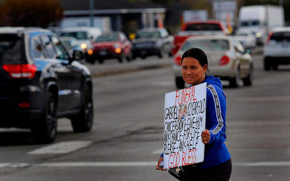 A woman who said her name is Teresa holds a sign with a picture of a child in a hospital bed and asking help for the funeral of the 12-year-old boy named Gabriel who died from cancer.