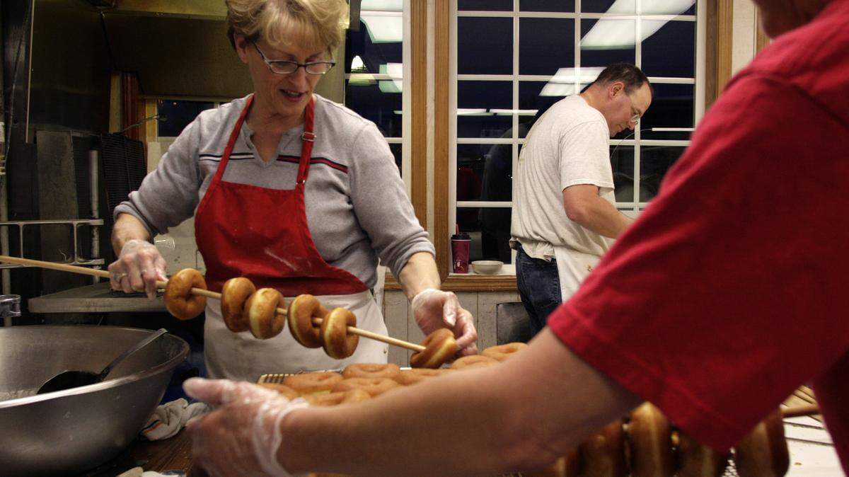 Spudnut owner Val Driver, left, and Barb Welch thread raised doughnuts onto dowels for glazing while Kevin Russell prepares cinnamon rolls and maple bars for frying.