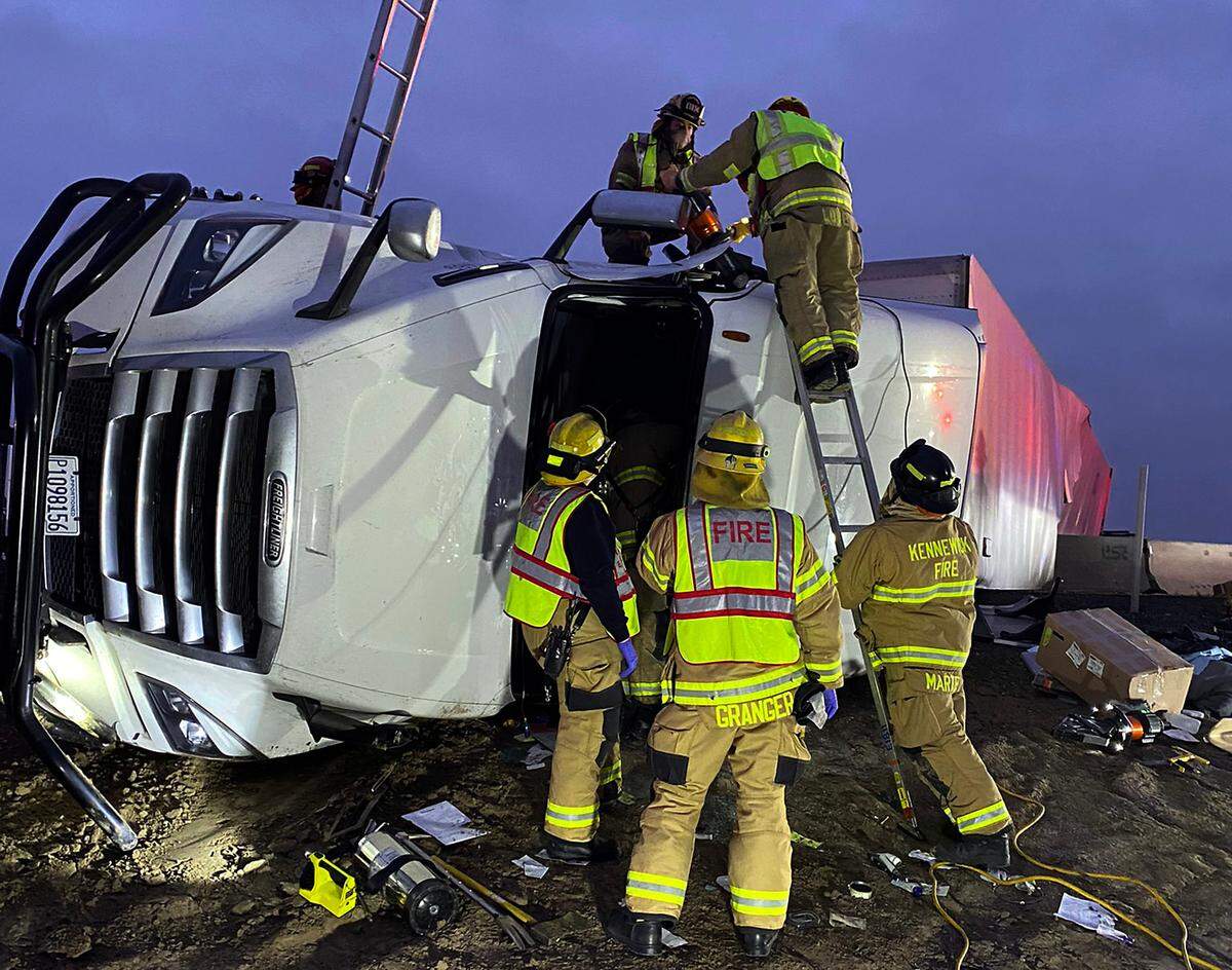 Firefighters work to free an injured driver from an overturned semi-truck early Thursday morning on Highway 395 at Ridgeline Drive in Kennewick.