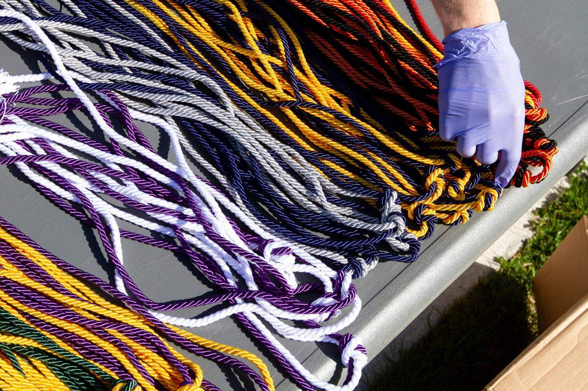 Mike Johnson, the principal of Delta High School, picks out cords to give seniors during a drive-thru cap and gown pick up at the school’s campus in Pasco on Thursday. Students stayed in their cars as some faculty and staff handed them their graduation garb while others honked and cheered from the parking lot.