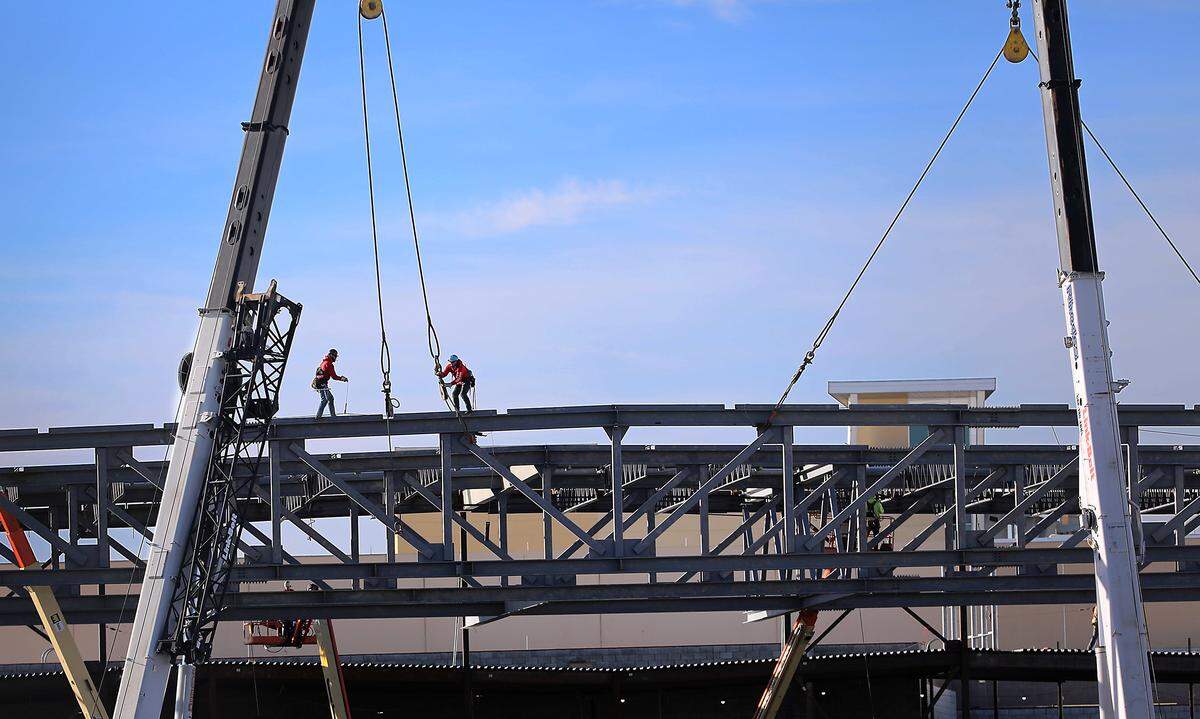 A pair of tethered iron workers disconnect the lift rigging from a 160-foot long steel roof support for the massive meeting hall addition that is part of the $71 million expansion at the Three Rivers Convention Center in Kennewick.