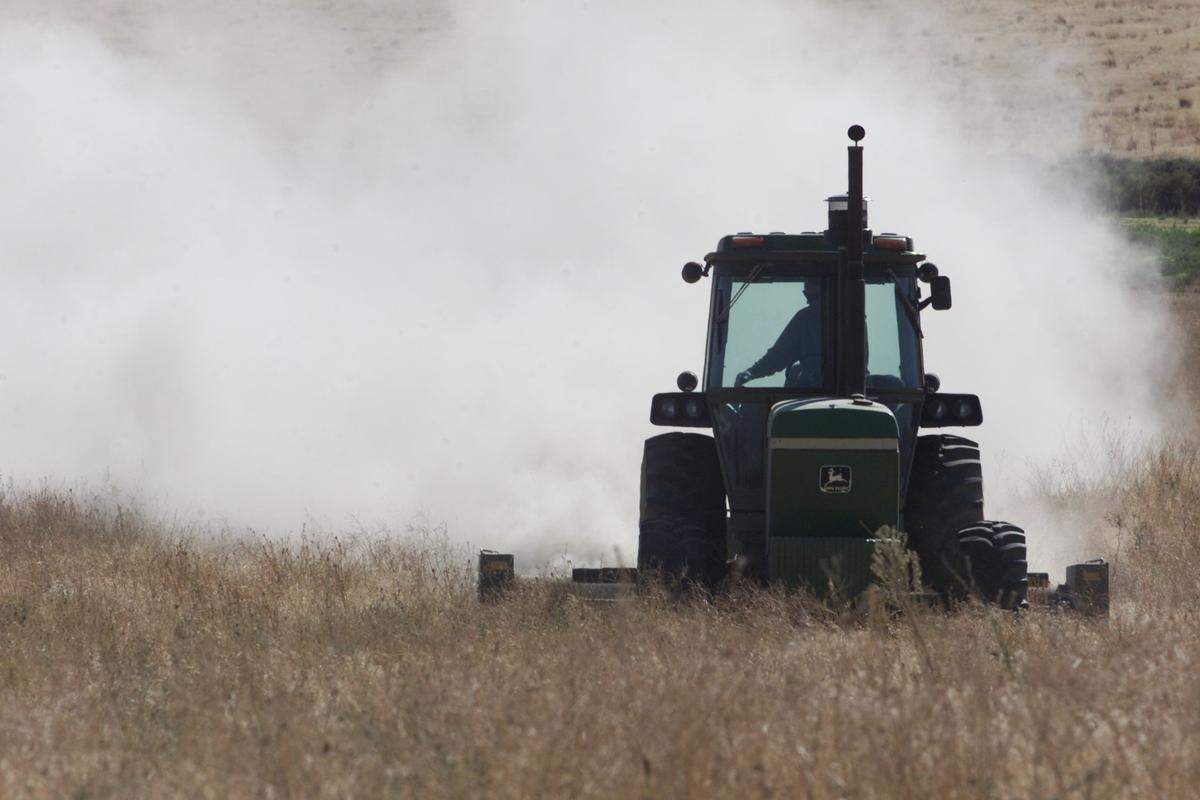 A cloud of dust is kicked up a tractor mowing vegetation in a field in southeast Kennewick.