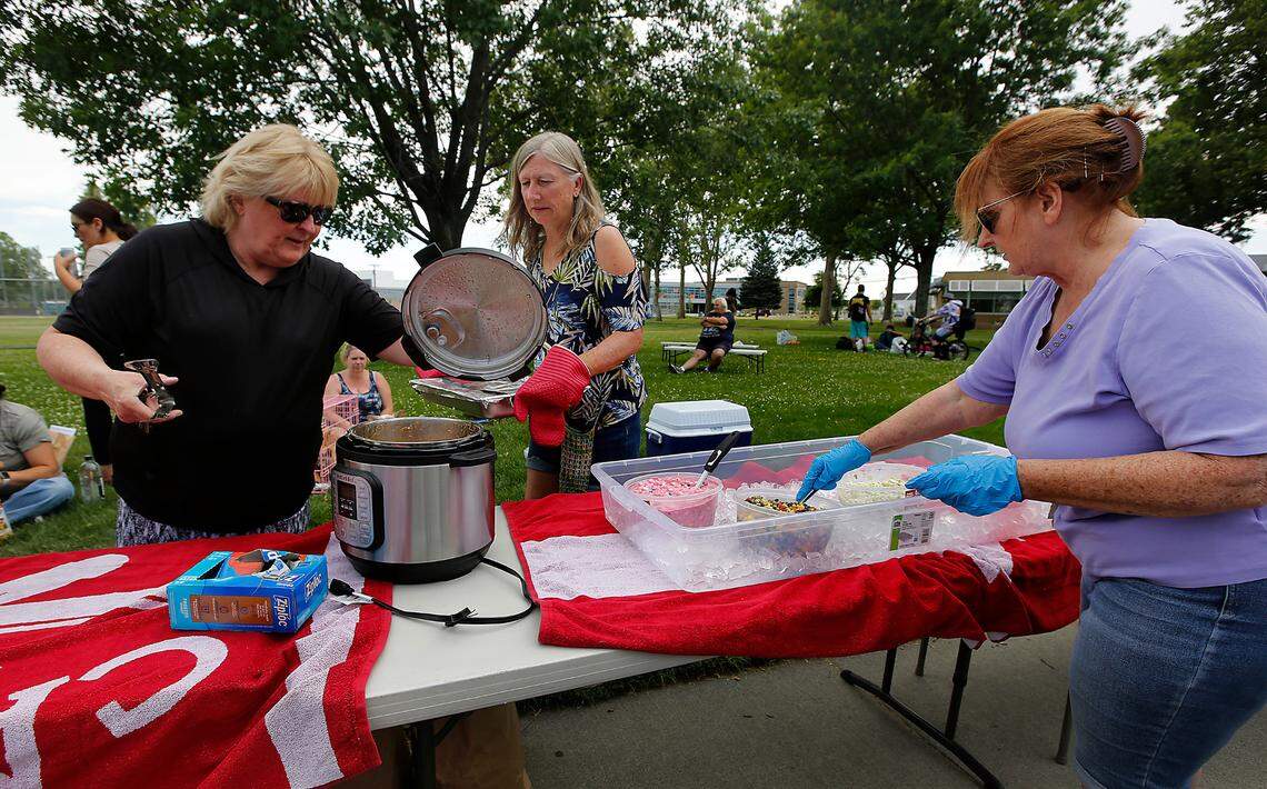 Volunteers Lana Franklin, Cindy Fish and Jenny Morse, from left, prepare to serve a free weekly meal on June 7, 2023 to a group of homeless gathered at Keewaydin Park in downtown Kennewick.