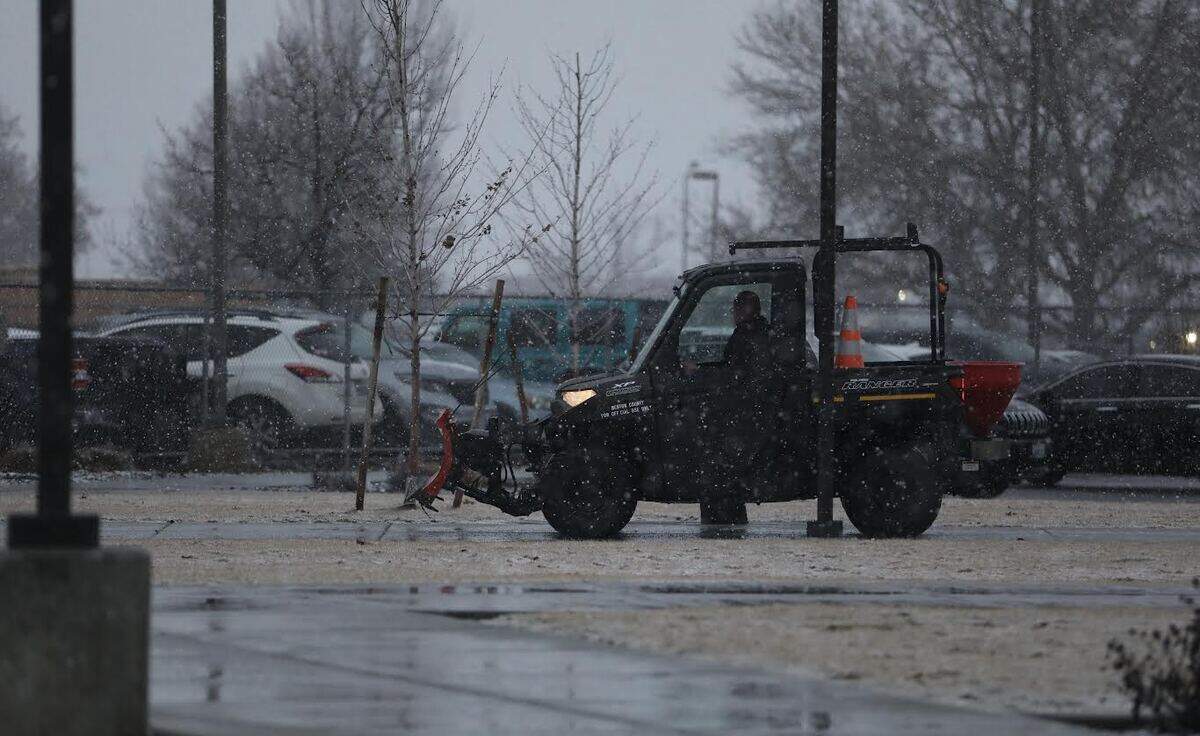 A Benton County worker spread ice melt at the Benton County Justice Center in Kennewick as snow fell before full light Thursday morning.