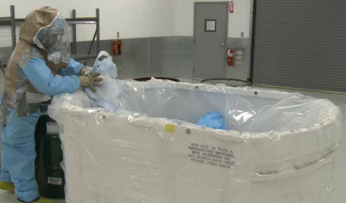 A Perma-Fix employee in protective gear works with waste.