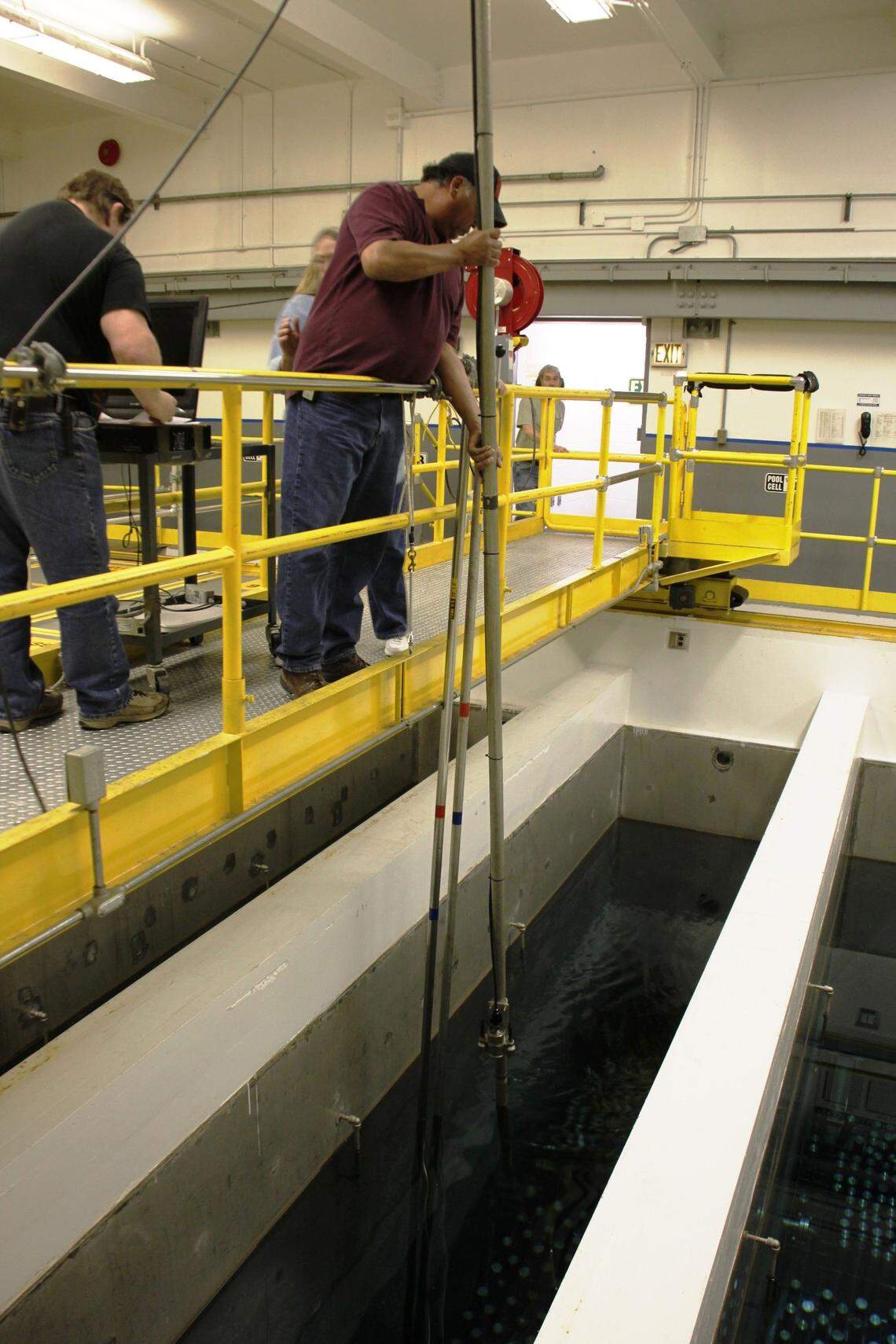 Workers inside the Waste Encapsulation and Storage Facility use long-handled tools to manipulate capsules of radioactive cesium and strontium stored beneath water.
