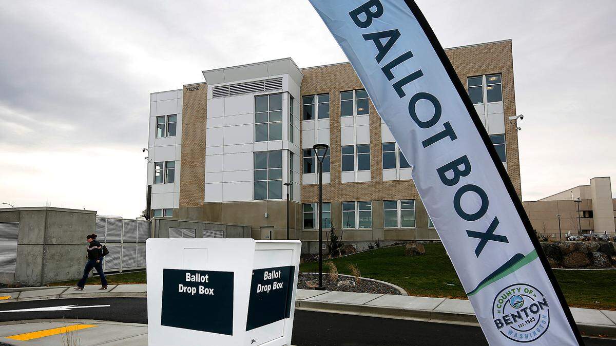 A woman walks past the drive-up and walk-up ballot drop box at the Benton County administration building in Kennewick. 