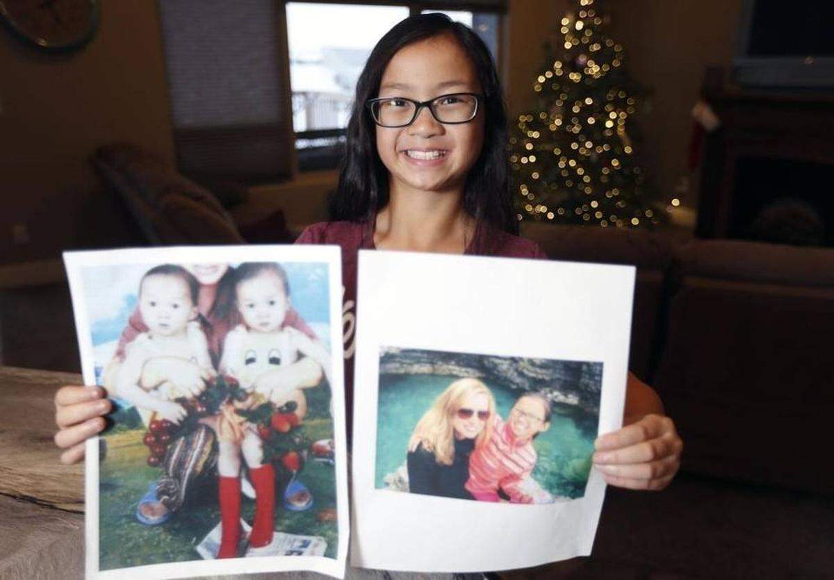 2016 HERALD FILE PHOTO — Richland fifth-grader Gracie Rainsberry, 10, holds a photo believed to be of her with her twin sister Audrey, from whom she was separated in China when they were 15 months old. The other photo is of Audrey with her adoptive mother in Wisconsin.