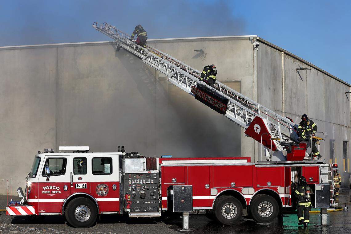 Firefighters climb to the roof on a Pasco aerial fire truck ladder as several area fire agencies work to extinguish an early morning warehouse fire.