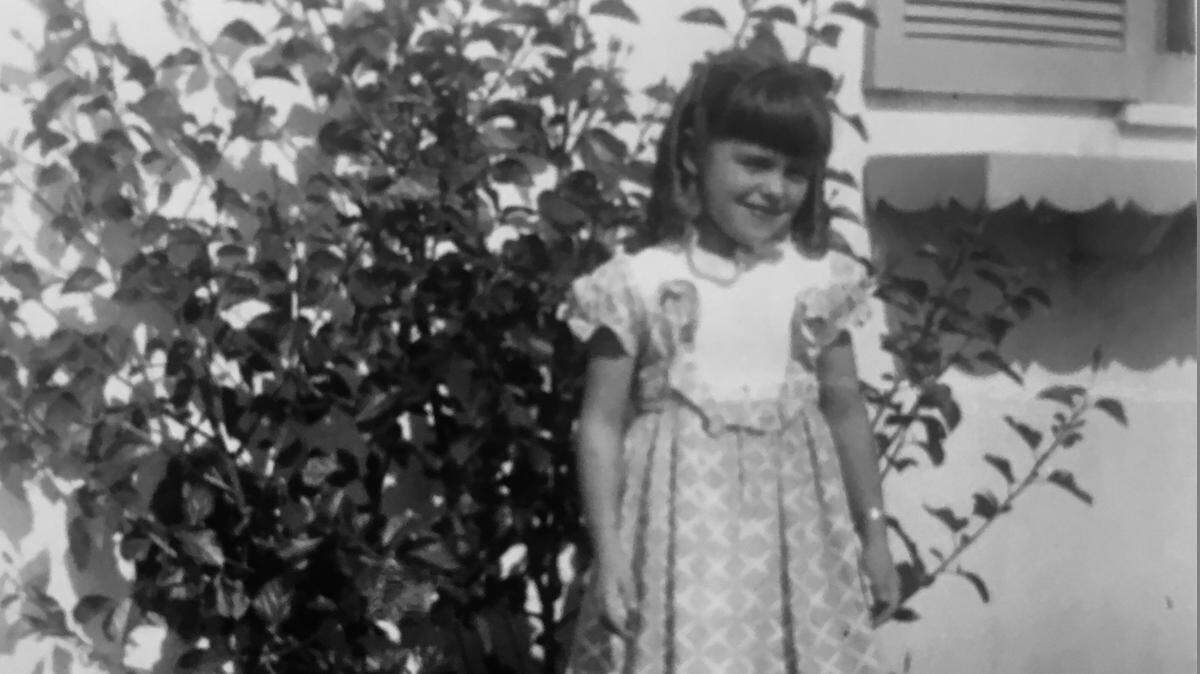 Lucy Luginbill, years ago, posing in front of her mother's flowers at her childhood home in California.