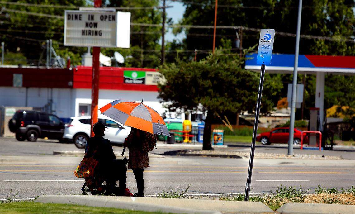 A pair of Ben Franklin Transit riders share a patch of shade under the umbrella they brought with them for their wait at the Ben Franklin Transit bus stop on West Vineyard Drive near Garfield Street in Kennewick.