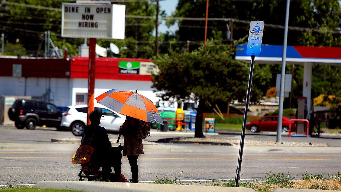A pair of Ben Franklin Transit riders share a patch of shade under the umbrella they brought with them for their wait at a Ben Franklin Transit bus stop in Kennewick.
