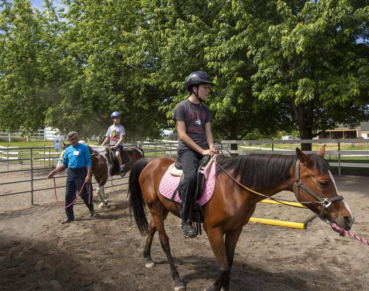 Students Jordan Lemmon, right, rides around the corral while a volunteer leads. Behind Lemmon, a TROT volunteer, Richard Alan, leads a horse while Hunter Ford rides.