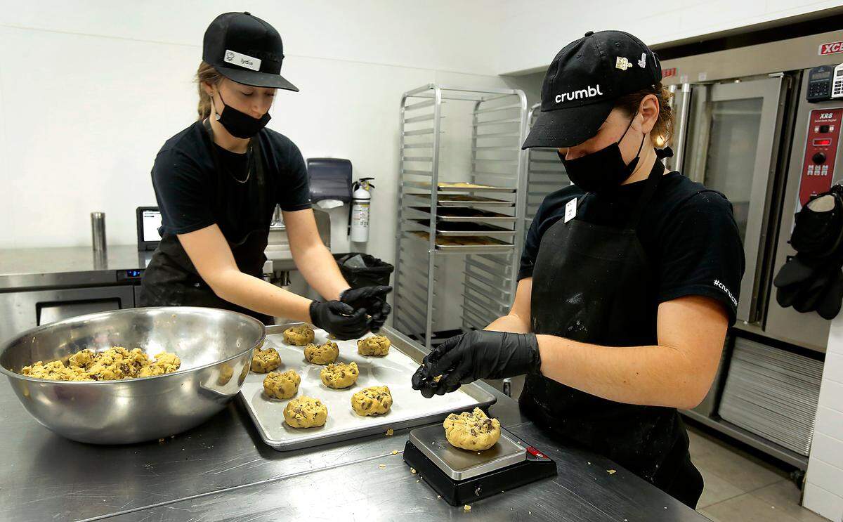Lydia Mortimer, left, and her co-worker Brie Aho, with Crumbl Cookies weigh out dough to make chocolate chip cookies this week at the Richland store. The fresh and tasty treats are one idea for last-minute Christmas gifts.