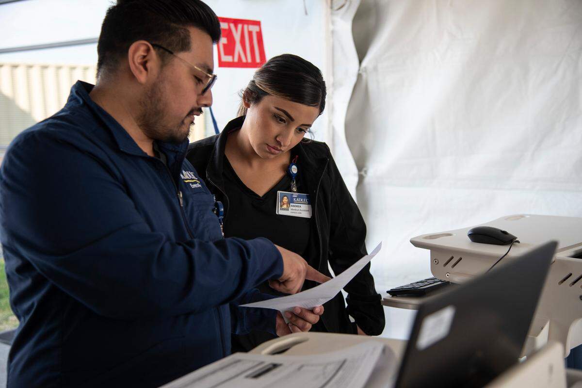 Medical assistants Lionel R., left, and Andrea Arevalo work at a testing tent set up behind the Kadlec Urgent Care in Kennewick on March 20. The tent is meant for Kadlec patients who are presenting flu-like symptoms to get tested for flu and COVID-19.