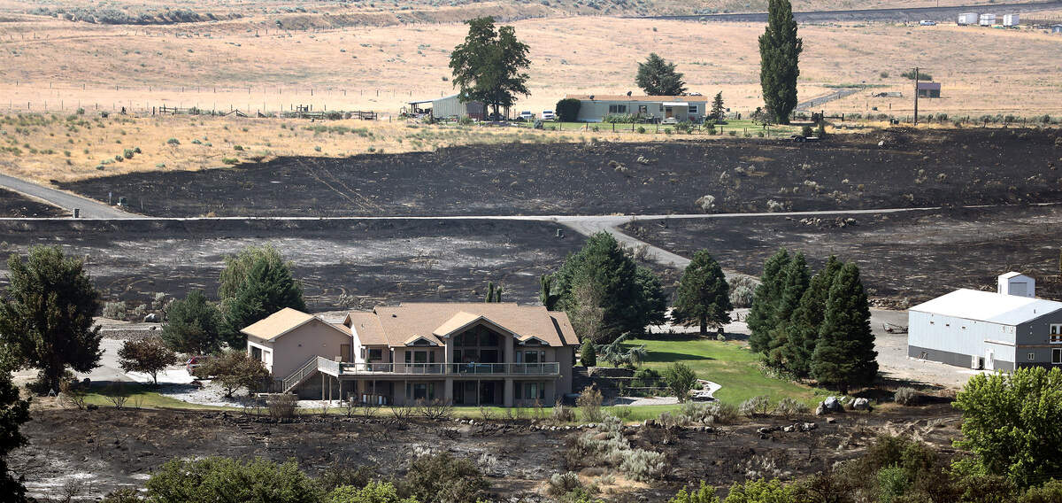 A home along the south side of the Yakima River between Benton City and Prosser appears intact Monday morning after fire burned around the property the previous day.