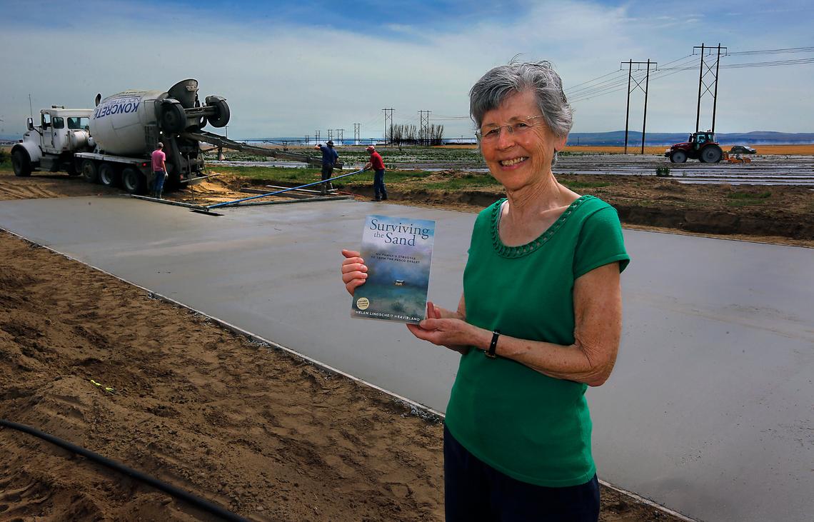 Author Helen Lingscheit Heavirland holds her book, Surviving the Sand: My Family’s Struggle to Farm the Pasco Desert, on the Franklin County farmland she moved to with her family as a seven-year-old in 1954. Heavirland is having a concrete slab poured on the farm for a manufactured home so she can soon move from Walla Walla back to where she grew up.