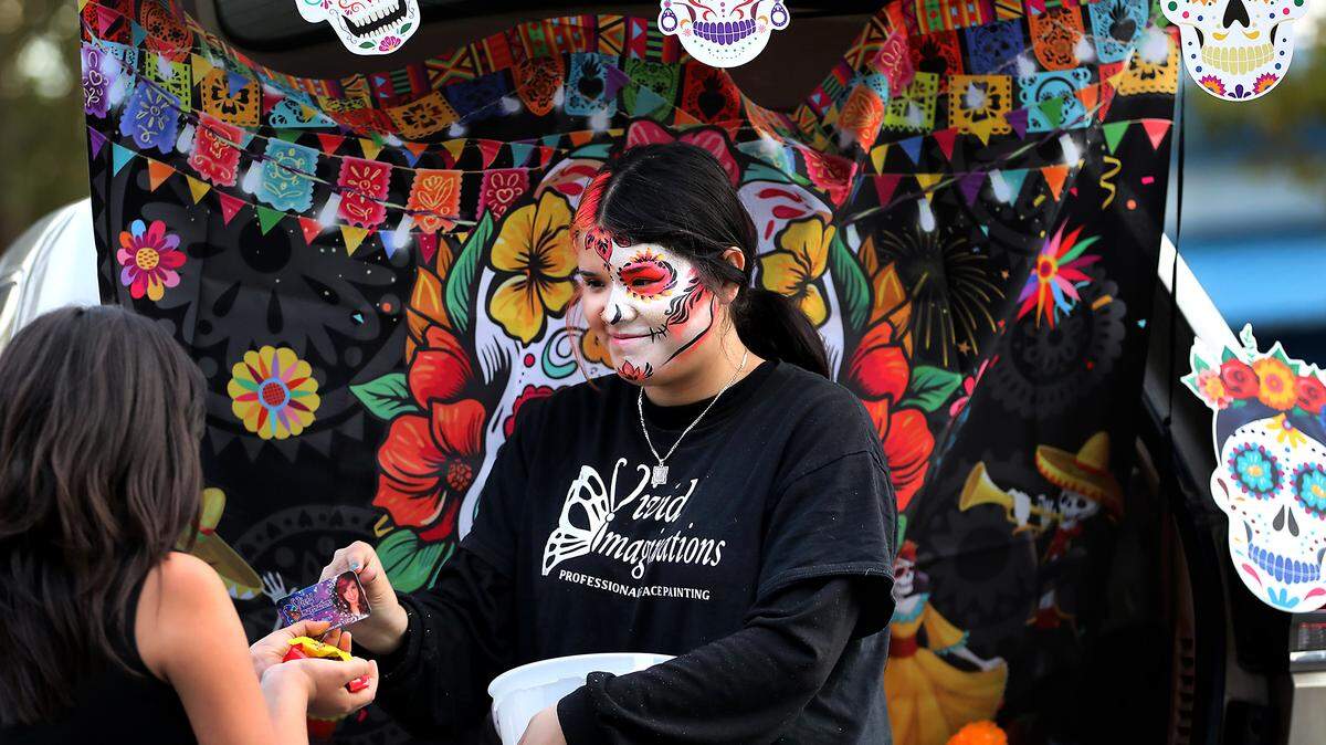 Jaquelin Centeño, an employee of Vivid Imagination Professional Face Painting, hands out goodies Thursday night during a Dia de Los Muertos Trunk-or-Treat event held at the Richland Public Library.