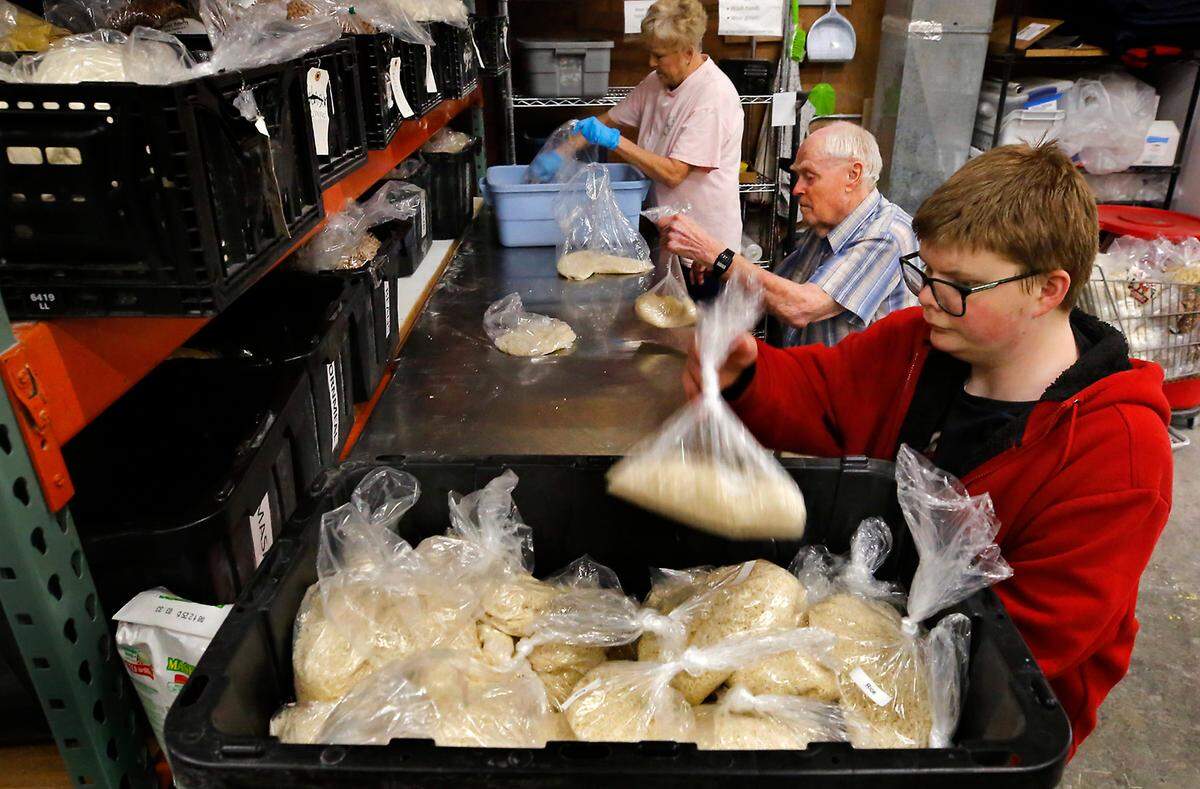 Volunteers Kim Knight, Gene Wallace and Peter Lavanwar, from left, work together in assembly line fashion sorting and weighing one pound bags of rice inside the Tri-Cities