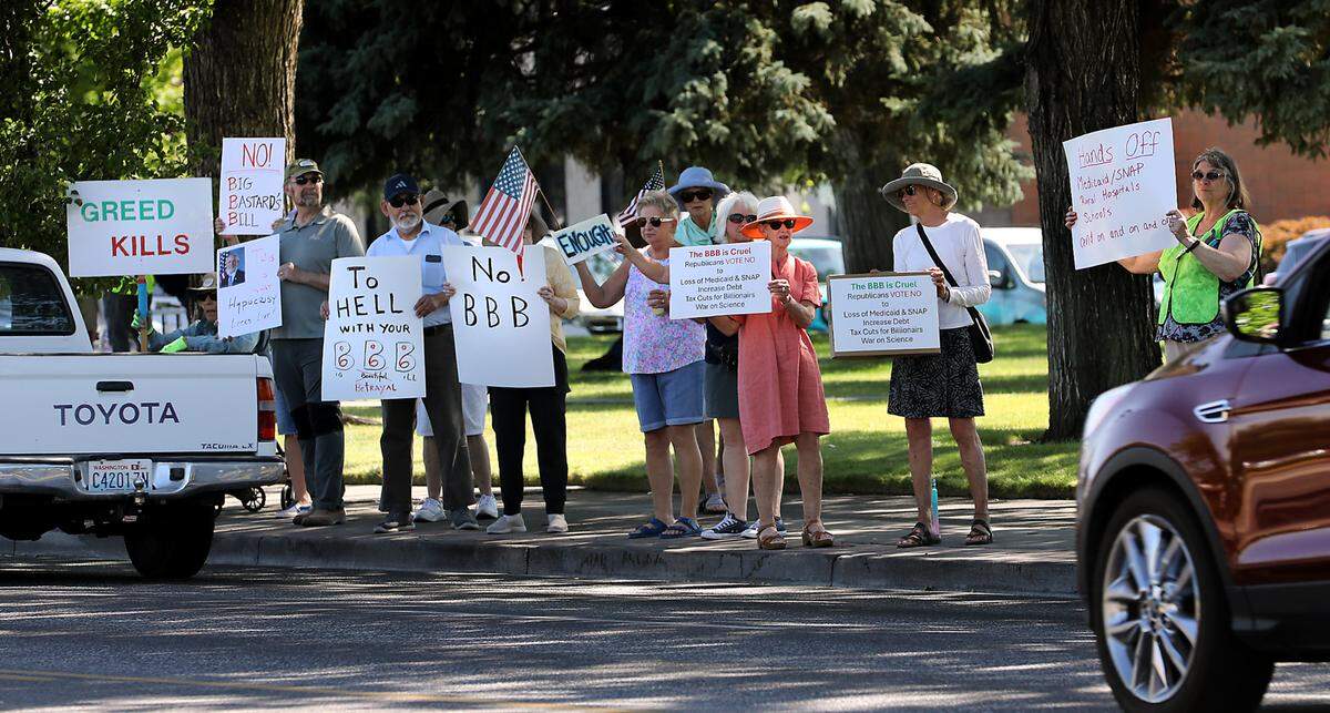 Protesters with Indivisible Tri-Cities stand on the sidewalk along George Washington Way near Richland’s John Dam Plaza to oppose the “One Big Beautiful Bill.”
