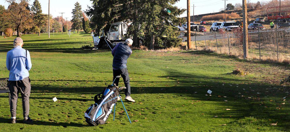 A pair of golfers tee off from the sixth hole past the wrecked semi-truck involved in a crash on Highway 240 in Kennewick. 