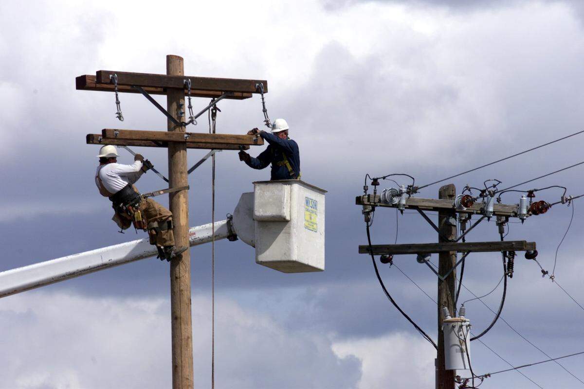 Damon Vermeire, left, and Bill Liles, employees of Wilson Construction Co. of Canby, Oe., work near the top of utility poles Tuesday afternoon on Columbia Center Boulevard just north of the Tapteal overpass. They are working on a wire relocation and improvement project of underground supply lines for Benton County Public Utility District.