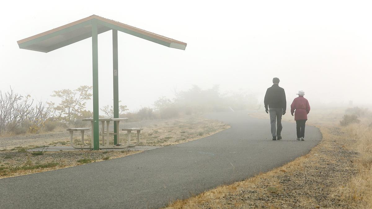 The Sacagawea Heritage Trail fades into dense fog Thursday morning walkers stroll past the North Fruitland Street access in downtown Kennewick. The chilly blanket rolled in at 9 a.m. mostly near the rivers. Morning patches of fog are expected to give way to sunny skies and highs in the mid to upper 60s through Tuesday, according to the National Weather Service.
