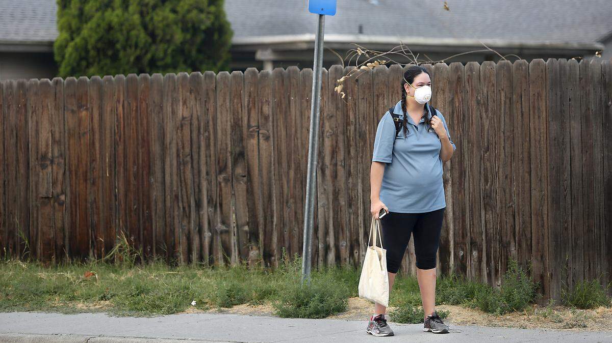 Jessica Vowels wears a mask to filter her breathing Tuesday morning while waiting at a transit bus stop on South Garfield Street in Kennewick. Vowels decided to wear the mask she bought at a hardware store after having trouble breathing because of the poor air quality in the Tri-Cities.