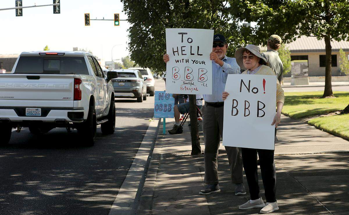 Protesters with Indivisible Tri-Cities stand on the sidewalk along George Washington Way near Richland’s John Dam Plaza to oppose the “One Big Beautiful Bill.”