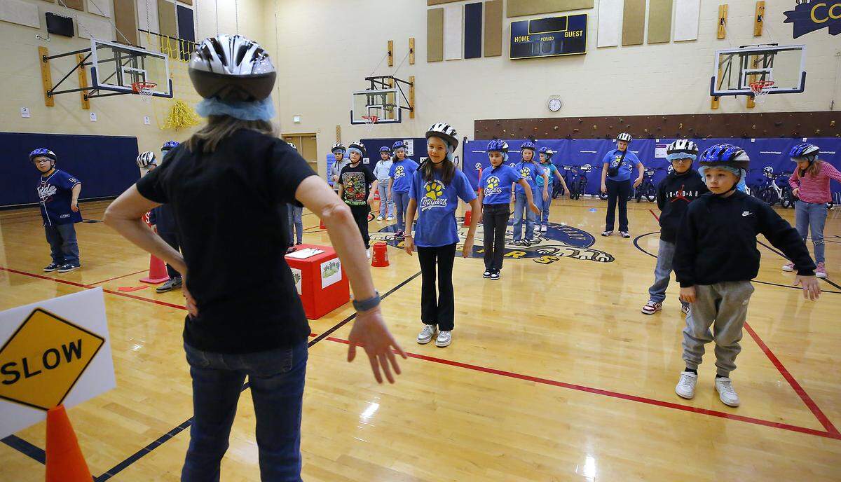 PE teacher Sue Swoboda demonstrates hand signals for the fifth-grade students in the Let's Go bicycle education and safety program in the gym at Cascade Elementary School in Kennewick.