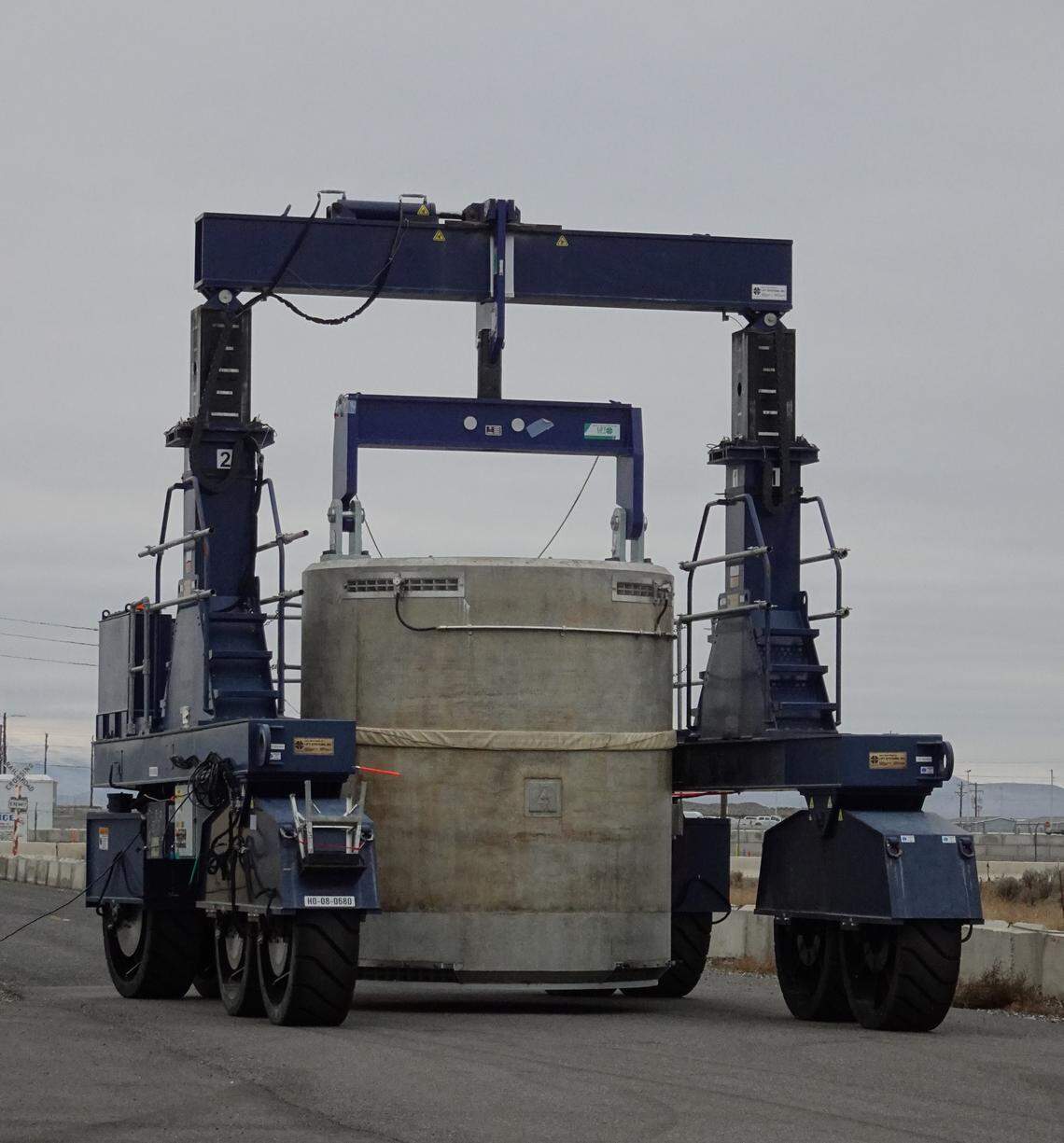 A transporter takes a concrete cask filled with radioactive capsules to an outdoor dry storage pad.