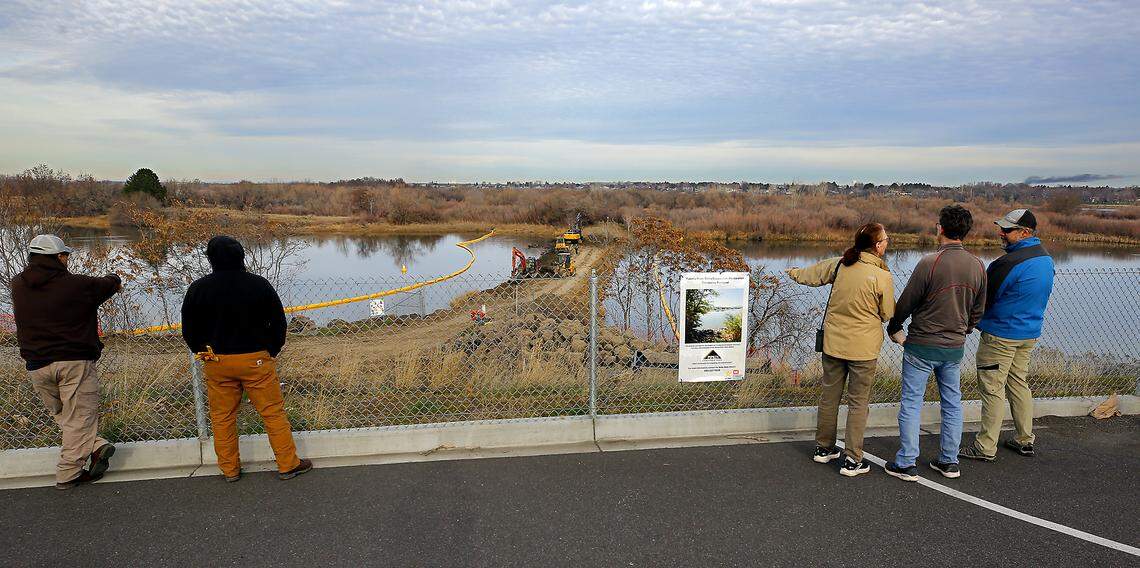 Groups of people gather on shore to wait for an excavator to remove scoops of dirt Tuesday afternoon to allow Yakima River water to begin flowing from behind the causeway to Bateman Island in Richland.