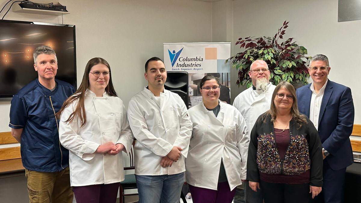 Derek Smith, left, executive chef instructor for Columbia Industries’ Opportunity Kitchen, and Michael Novakovich, right, president and CEO, pose with the newest graduates of the training program .