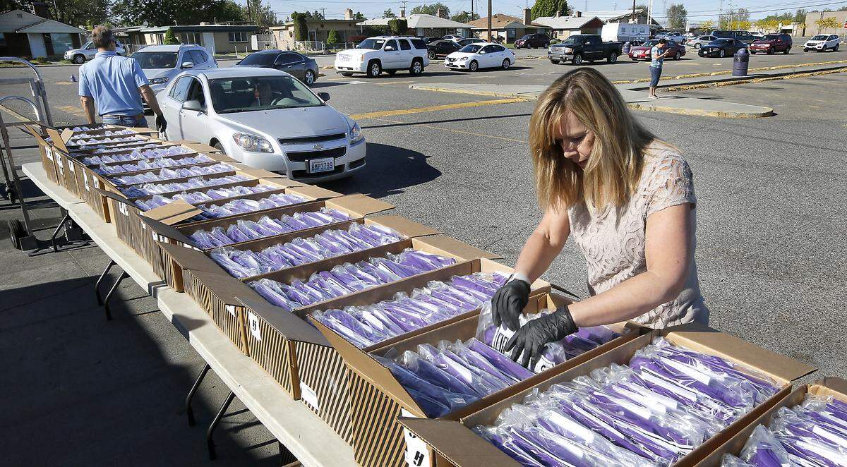 Susan Heckel and her husband, Jim, of the Herff Jones academic achievement company work together Friday distributing caps and gowns to Pasco High seniors and their family members during a parking lot distribution at the school. The students were able to stay in their cars to maintain coronavirus social distancing guidelines during the event which included a cheer zone filled with teachers, staff and administrators. Watch a video at: tricityherald.com/videos