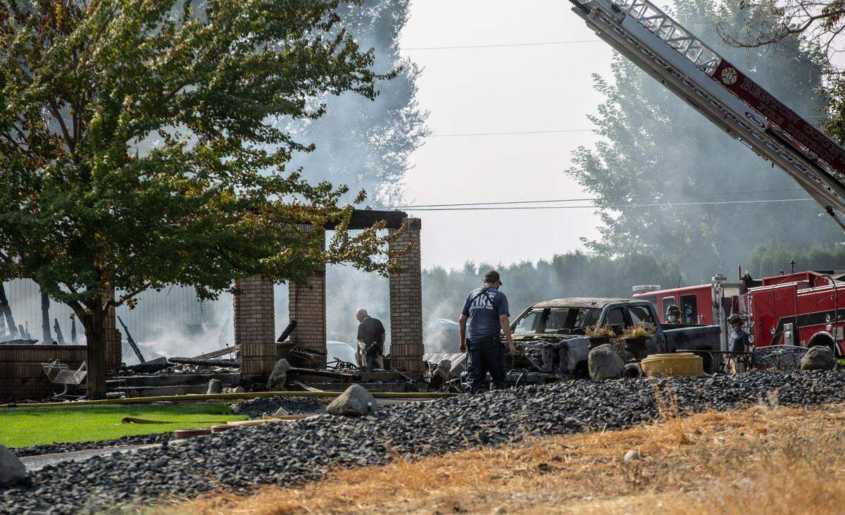 Benton County Coroner Bill Leach, left, examines a scene off East Finley Road where Bob Zlatich was killed by a neighbor who then burned his home on Aug. 25, 2021.