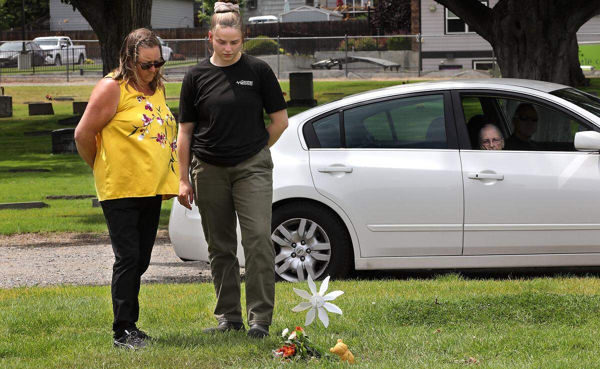 Benton County Coroner employees Debbie Hollis, left, and Jlyn Timmons pause of a moment of quiet reflection after placing flowers decorate on the restored gravesite of Baby Doe moments after Thursday's reinterment ceremony at Richland’s Resthaven Cemetery.