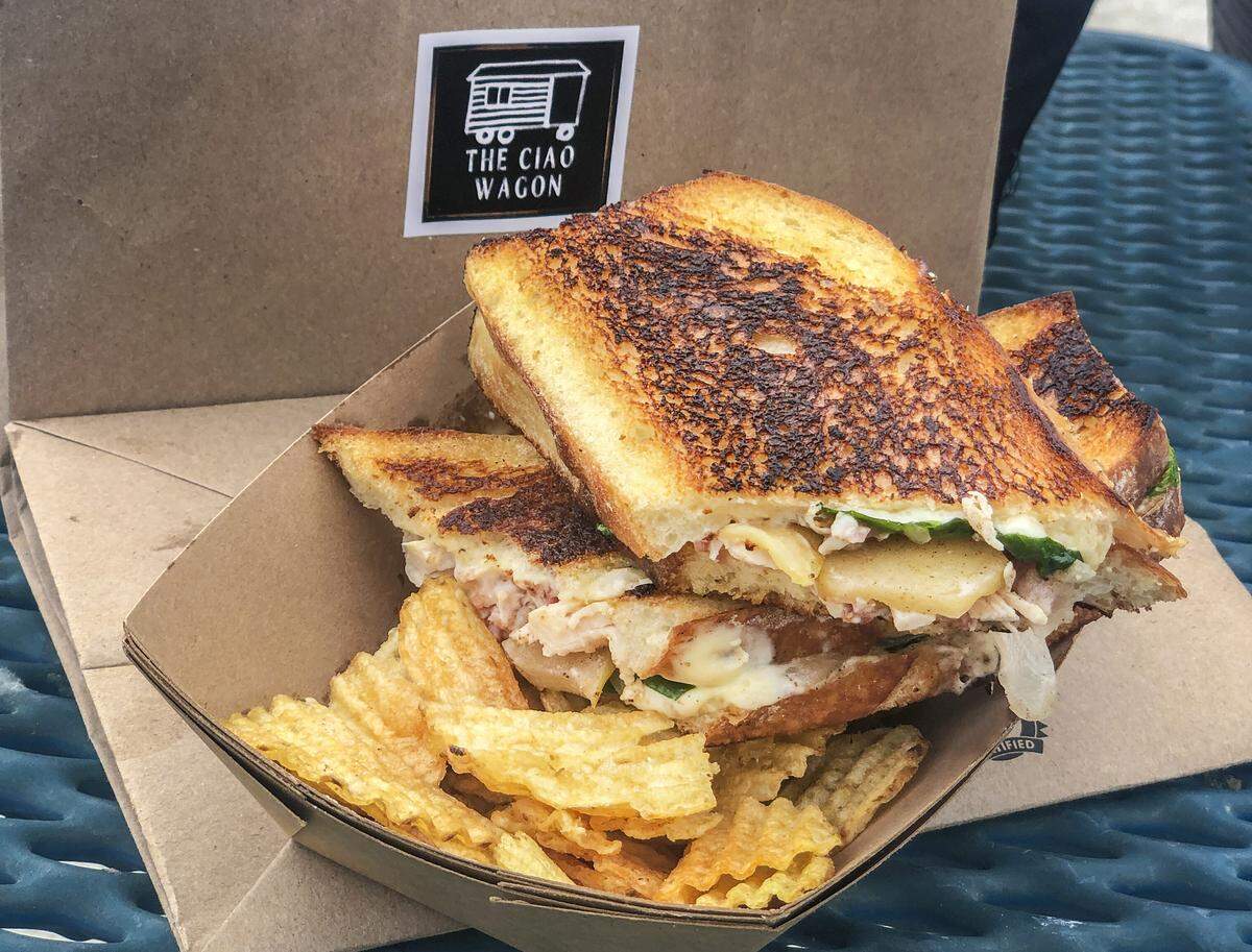Chicken smash sandwich with brie, chicken, basil, sliced apples on french bread and a side of chips.