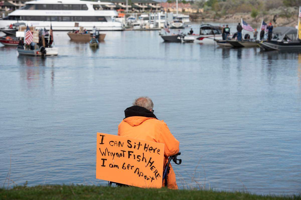 Al Bernicker, 74, of Richland sits on his walker with a protest sign at the Columbia Point Park Marina in Richland on Saturday. “Closing the state grounds is one thing but closing fishing down everywhere doesn’t strike me as right,” he said.