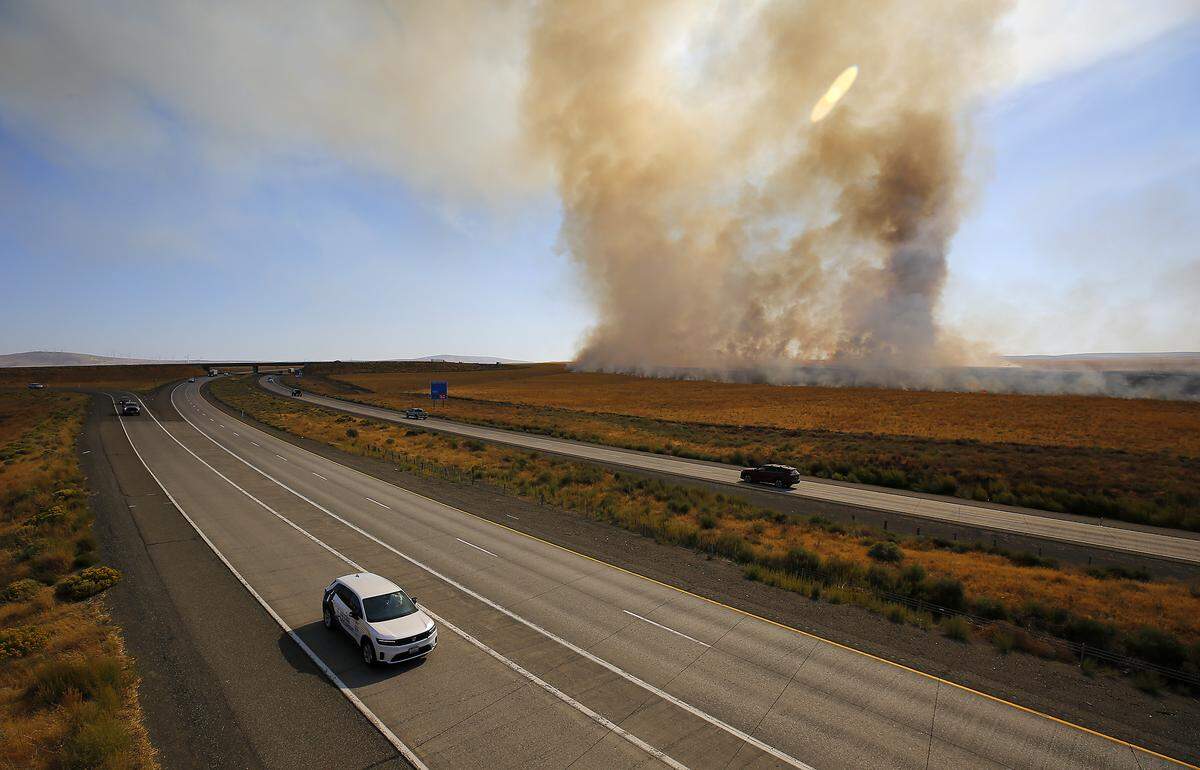 Traffic continues to flow past as firefighters battle a wildfire Thruday afternoon along the south side of Interstate 82 off Christensen Road just south of Kennewick.